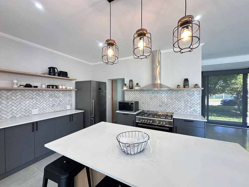 Modern kitchen featuring a central island, herringbone tile backsplash, floating timber shelving, and high-end stainless steel appliances with contemporary pendant lighting.