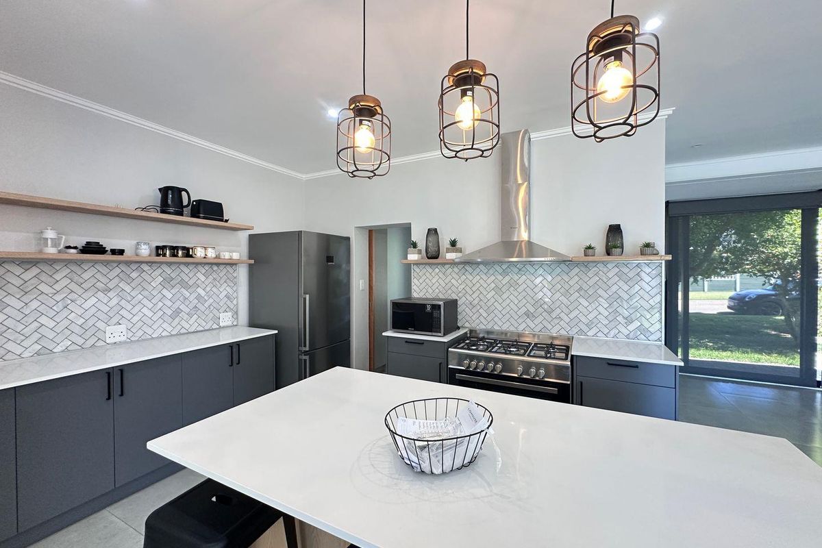 Modern kitchen featuring a central island, herringbone tile backsplash, floating timber shelving, and high-end stainless steel appliances with contemporary pendant lighting.