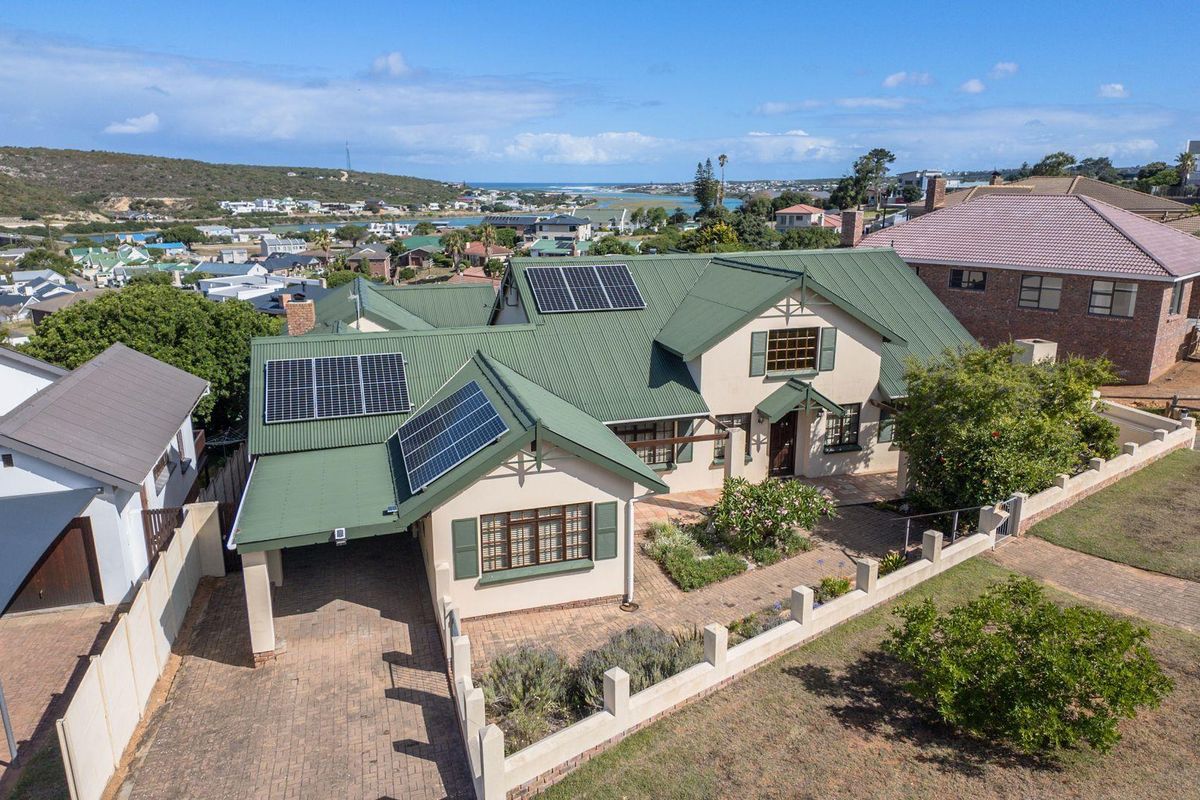 Aerial view of a residential property featuring a green metal roof with solar panels, a paved driveway, and a front garden with boundary wall.
