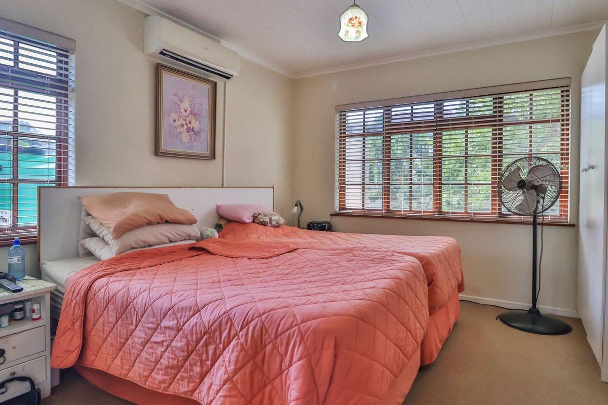 A well-lit bedroom featuring a built-in wardrobe, air conditioning unit, and large windows with timber venetian blinds.
