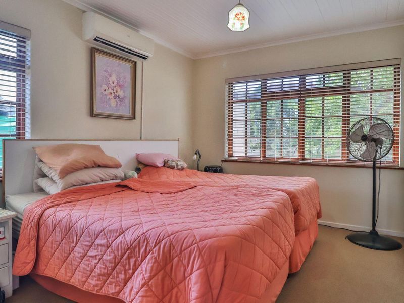 A well-lit bedroom featuring a built-in wardrobe, air conditioning unit, and large windows with timber venetian blinds.