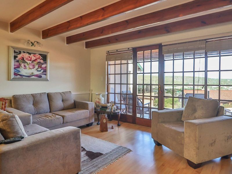A comfortable living room featuring exposed timber ceiling beams, laminate flooring, and large timber-framed glass doors that provide natural light and access to the outdoors.