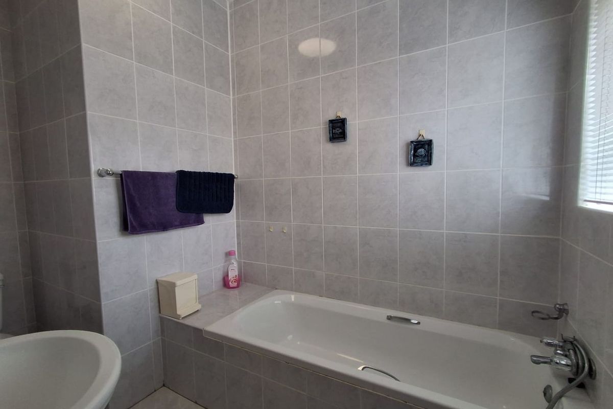 A functional bathroom featuring a built-in bathtub with a mixer tap, handheld shower attachment, and neutral wall tiling throughout.