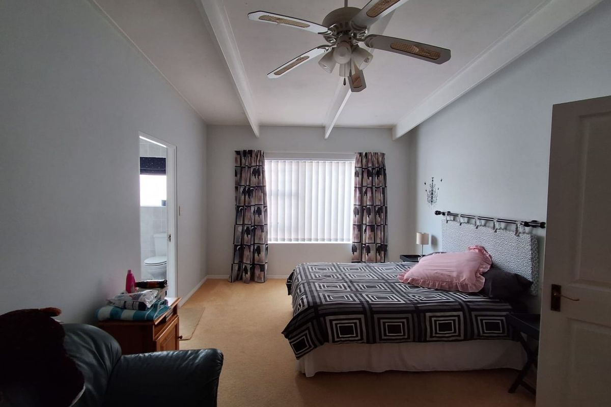 A spacious bedroom featuring exposed ceiling beams, a central ceiling fan, and carpeted flooring, with an adjoining en-suite bathroom visible.