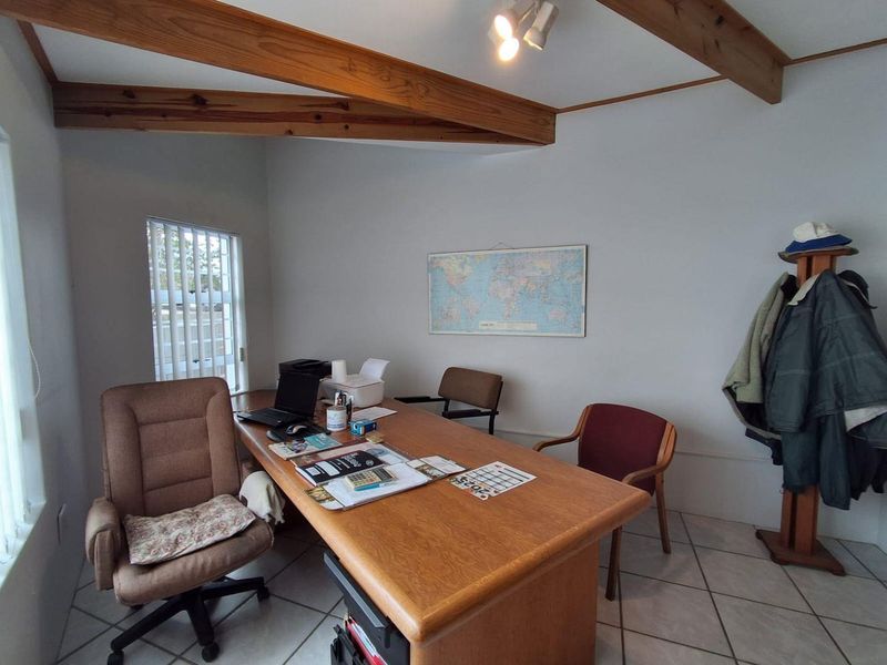 A functional home office featuring exposed timber ceiling beams, ceramic floor tiling, and natural light through vertical blinds.