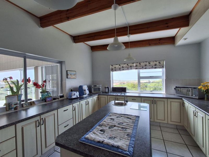 Spacious kitchen featuring an island, exposed timber ceiling beams, tiled flooring, and ample cabinetry with laminate countertops, offering pleasant natural light and views.