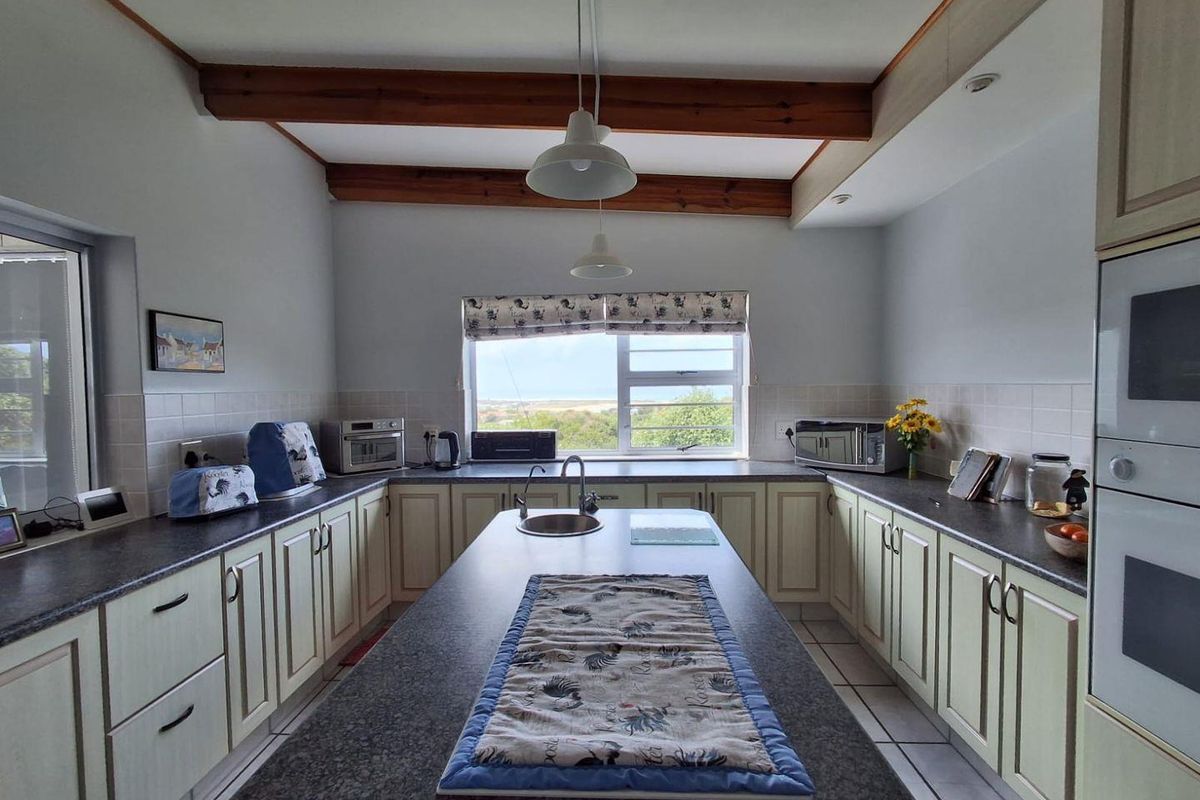 Spacious kitchen featuring a central island, built-in oven and microwave, tiled backsplash, and exposed timber ceiling beams with views through the window.