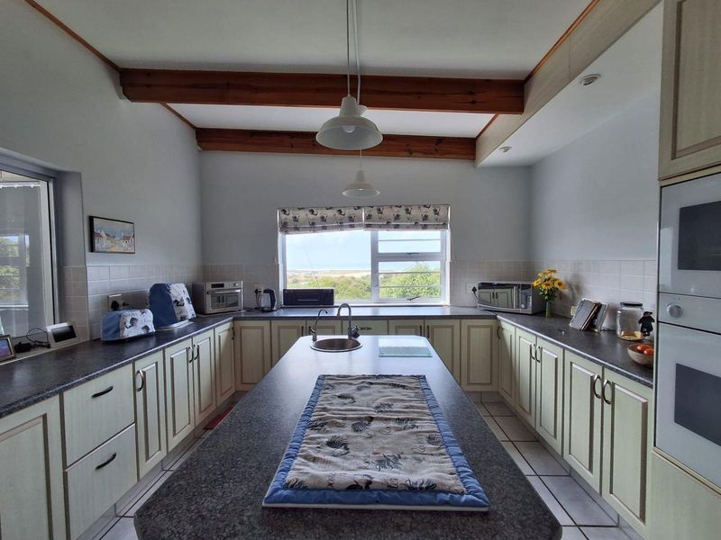 Spacious kitchen featuring a central island, built-in oven and microwave, tiled backsplash, and exposed timber ceiling beams with views through the window.