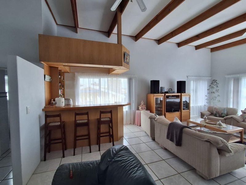 Spacious open-plan living area featuring a built-in bar, vaulted ceilings with exposed timber beams, and neutral tiled flooring throughout.