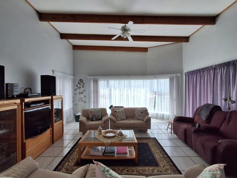 Spacious living room featuring high vaulted ceilings with exposed timber beams, tiled flooring, and a large window providing ample natural light.