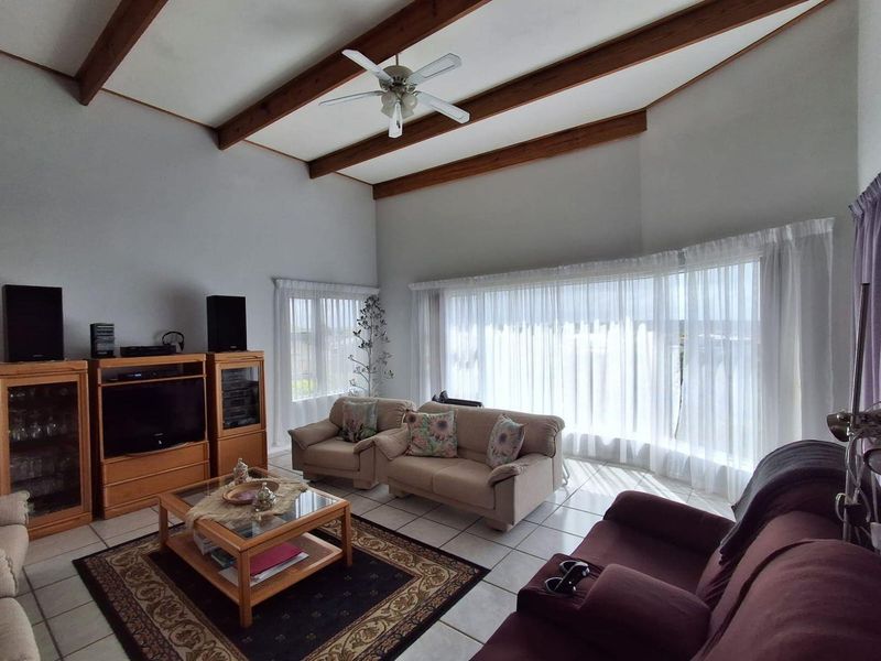 Spacious living room featuring a vaulted ceiling with exposed timber beams, large bay windows for natural light, and neutral ceramic floor tiles.