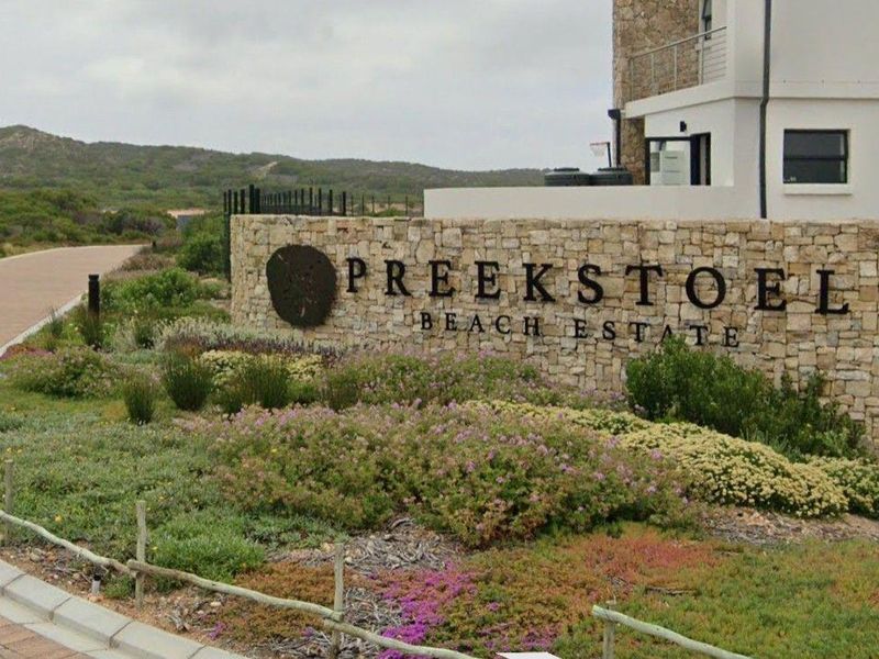 Entrance view of Preekstoel Beach Estate featuring a stone-clad boundary wall, professional landscaping, and paved access road.