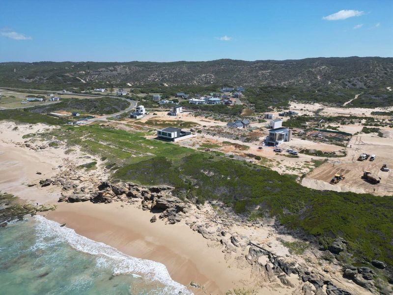 An aerial view of a coastal residential development situated along a sandy beach and rocky shoreline, showcasing the surrounding natural landscape.