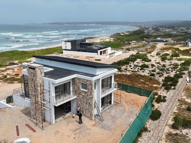 Aerial view of a modern coastal residence under construction, featuring stone cladding, flat roof design, and expansive ocean views.