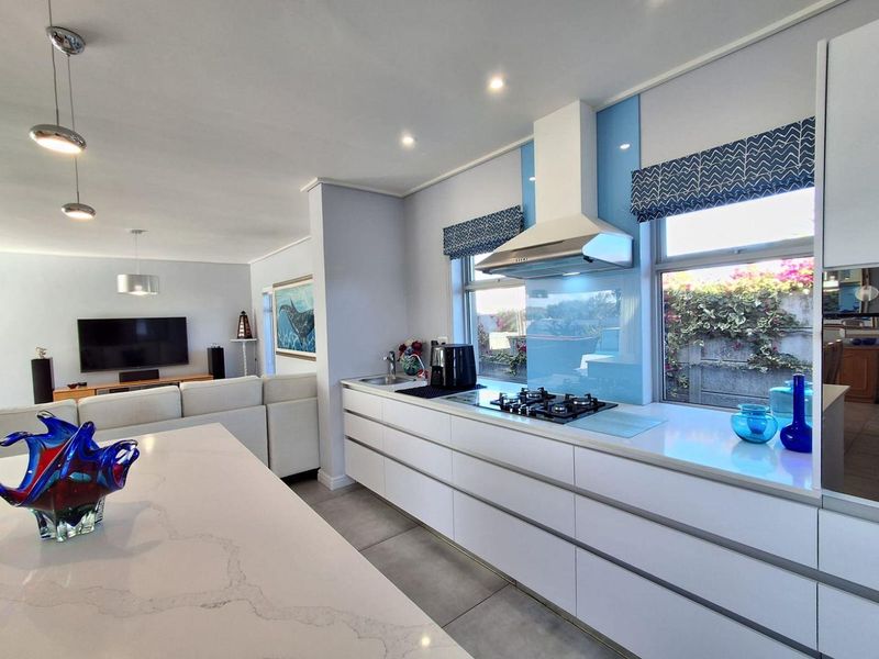 Modern open-plan kitchen featuring sleek white cabinetry, quartz countertops, a gas hob, and a central island, seamlessly flowing into the adjacent living area.