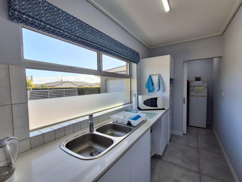 A functional scullery featuring a double stainless steel sink, tiled splashback, and ample built-in cabinetry with tiled flooring.