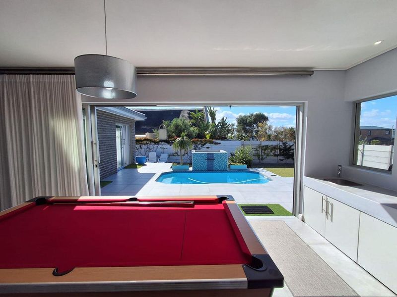 Open plan entertainment area featuring built-in cabinetry with sink, flowing seamlessly through large sliding doors to a patio and swimming pool area.