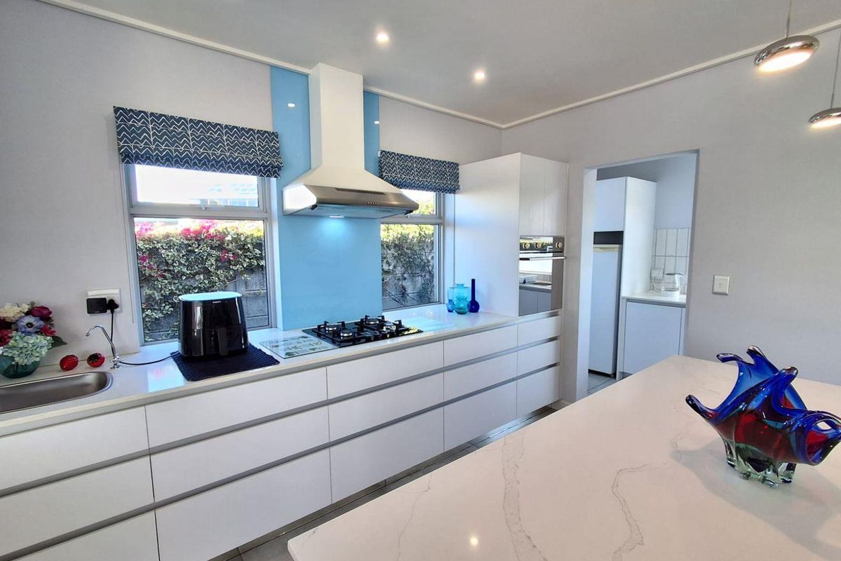 Modern kitchen featuring sleek handleless cabinetry, quartz countertops, a gas hob with extractor fan, and a separate scullery area.