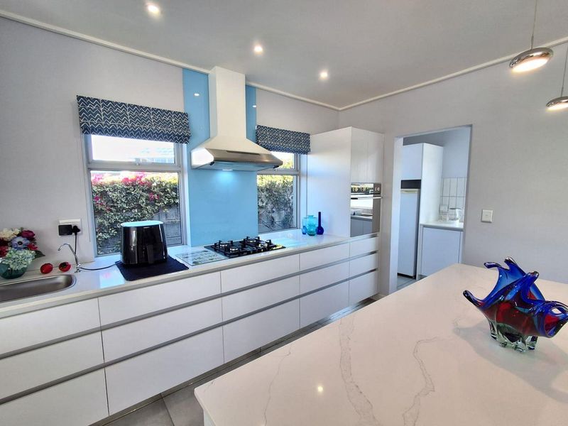 Modern kitchen featuring sleek handleless cabinetry, quartz countertops, a gas hob with extractor fan, and a separate scullery area.