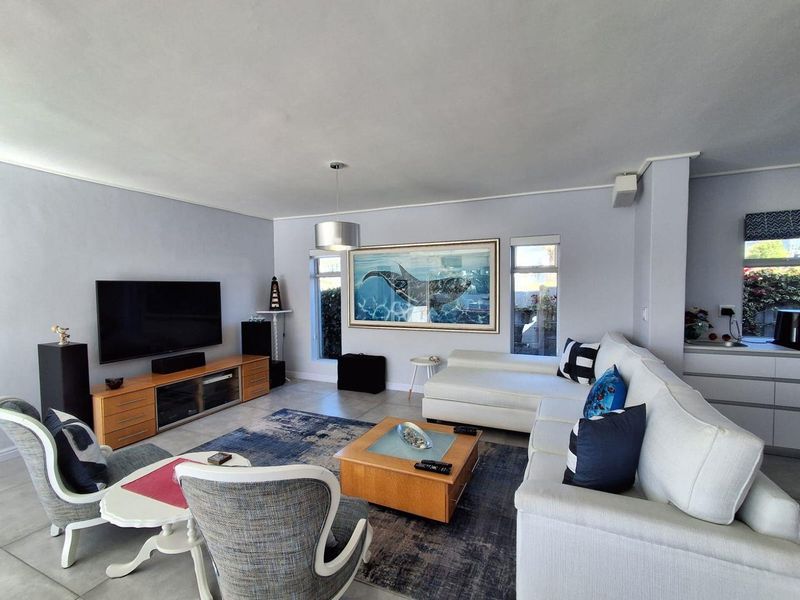 A spacious and well-lit living room featuring neutral wall tones, tiled flooring, and large windows that provide ample natural light.