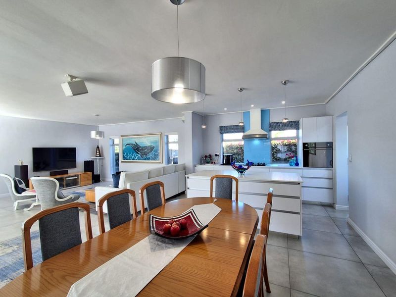 Spacious open-plan living area featuring a modern kitchen with a central island, built-in appliances, and tiled flooring, seamlessly flowing into the dining and lounge space.