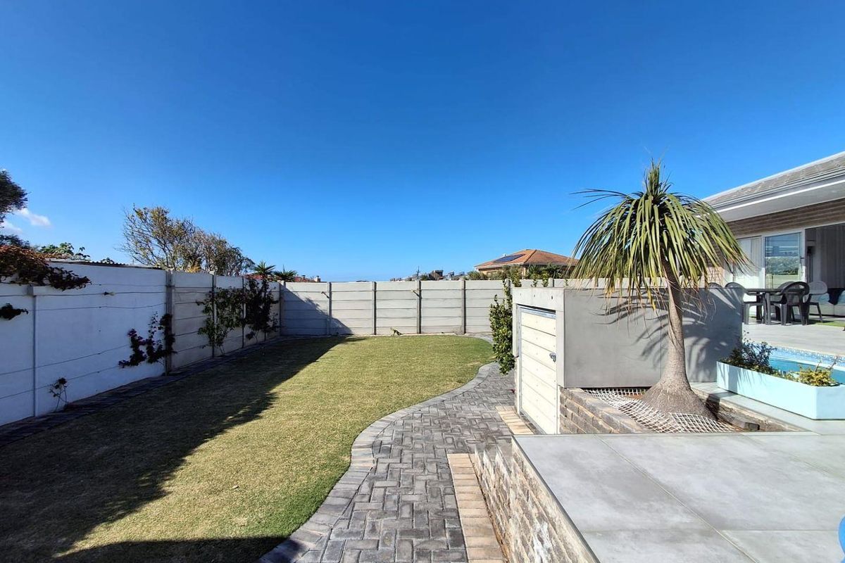 A well-maintained rear garden featuring a paved walkway, a swimming pool, and a secure precast concrete boundary wall.