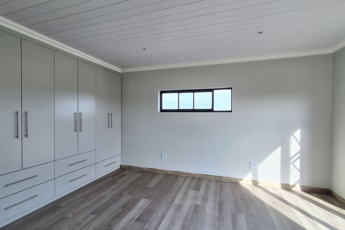 A bright, modern bedroom featuring neutral walls, light wood-look laminate flooring, a tongue and groove ceiling, and extensive built-in cupboard storage.