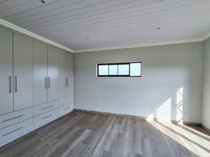 A bright, modern bedroom featuring neutral walls, light wood-look laminate flooring, a tongue and groove ceiling, and extensive built-in cupboard storage.