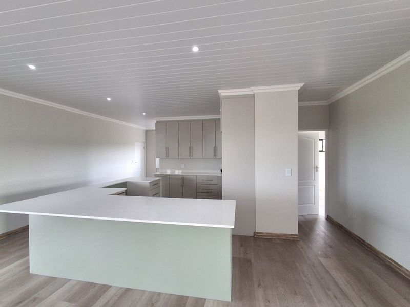 Modern, open-plan kitchen featuring a large island, neutral cabinetry, laminate flooring, and a clean, contemporary aesthetic.