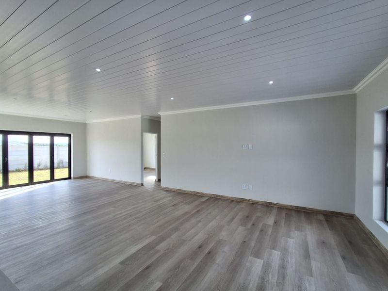 A bright, spacious, and modern open-plan living area featuring neutral finishes, recessed lighting, and durable timber-look flooring with access to the outdoors.