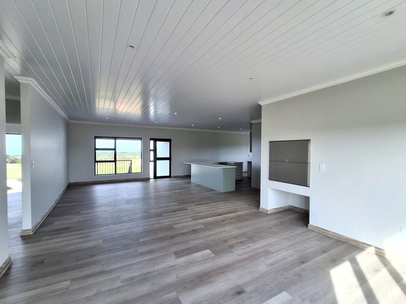 Spacious open-plan living area featuring modern laminate flooring, a tongue and groove ceiling with recessed lighting, and a built-in indoor braai.
