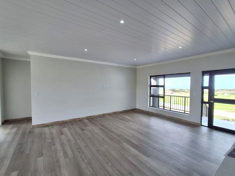 A bright and spacious living area featuring modern laminate flooring, a clean tongue and groove ceiling with recessed lighting, and large aluminium framed windows.