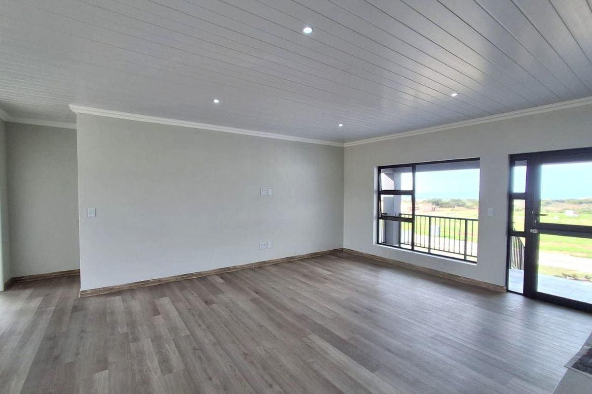 A bright and spacious living area featuring modern laminate flooring, a clean tongue and groove ceiling with recessed lighting, and large aluminium framed windows.