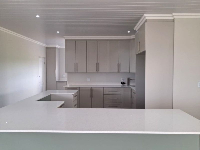 A modern, clean kitchen featuring neutral-toned cabinetry, quartz countertops, an island, and recessed lighting, presenting a well-maintained and contemporary aesthetic.