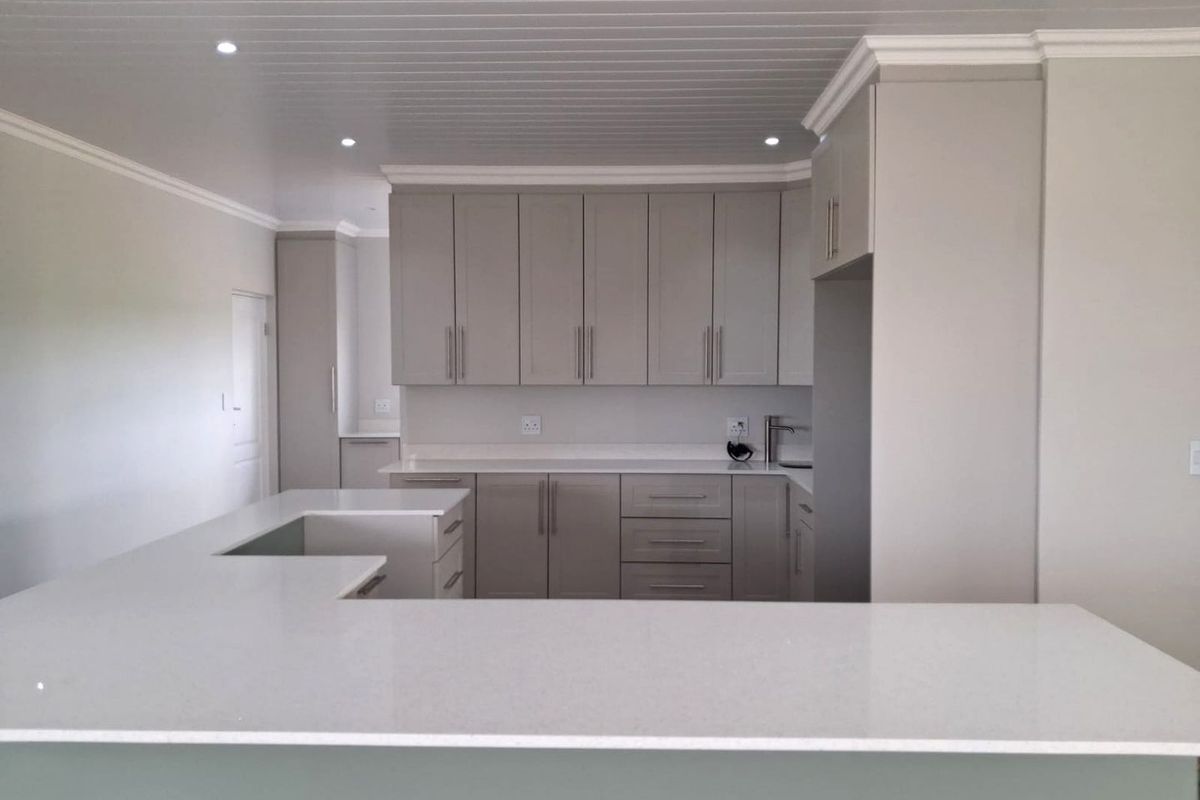 A modern, clean kitchen featuring neutral-toned cabinetry, quartz countertops, an island, and recessed lighting, presenting a well-maintained and contemporary aesthetic.