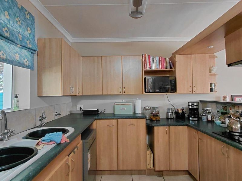 Functional kitchen featuring light wood-finish cabinetry, dark laminate countertops, a double basin sink, and a built-in gas hob with an extractor fan.