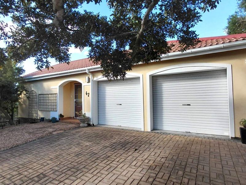 Front elevation of a residential house featuring a double garage with roll-up doors, a paved driveway, and a covered entrance with security gate.