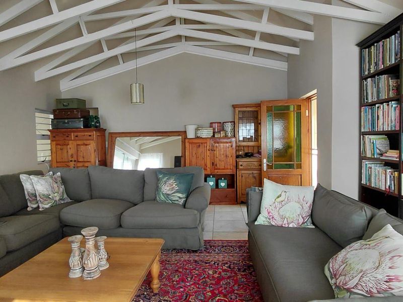 Spacious living room featuring high vaulted ceilings with exposed white timber trusses, tiled flooring, and a large built-in floor-to-ceiling bookshelf.