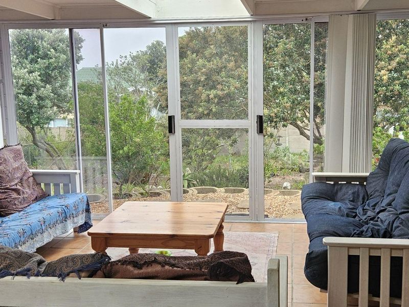 A bright, enclosed patio area featuring tiled flooring, exposed beam ceilings, and large sliding glass doors that provide views of the garden.