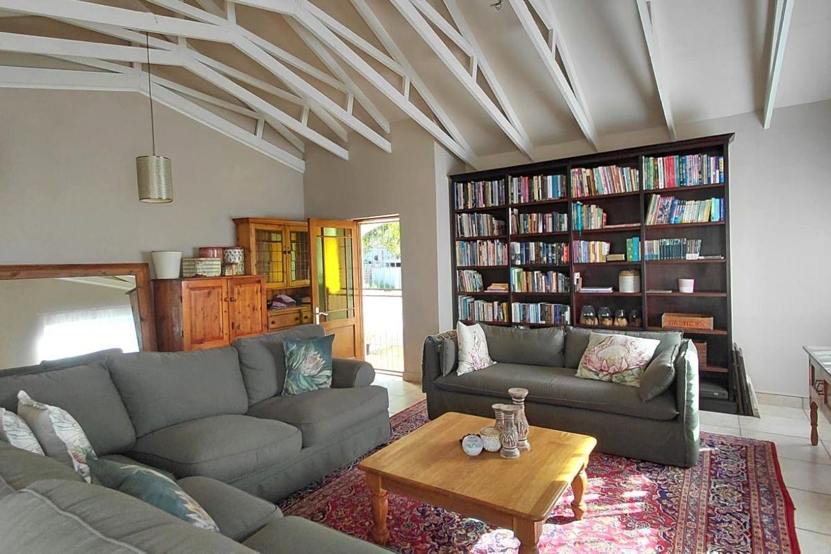 Spacious living room featuring a high vaulted ceiling with exposed white trusses and a large built-in floor-to-ceiling bookshelf.