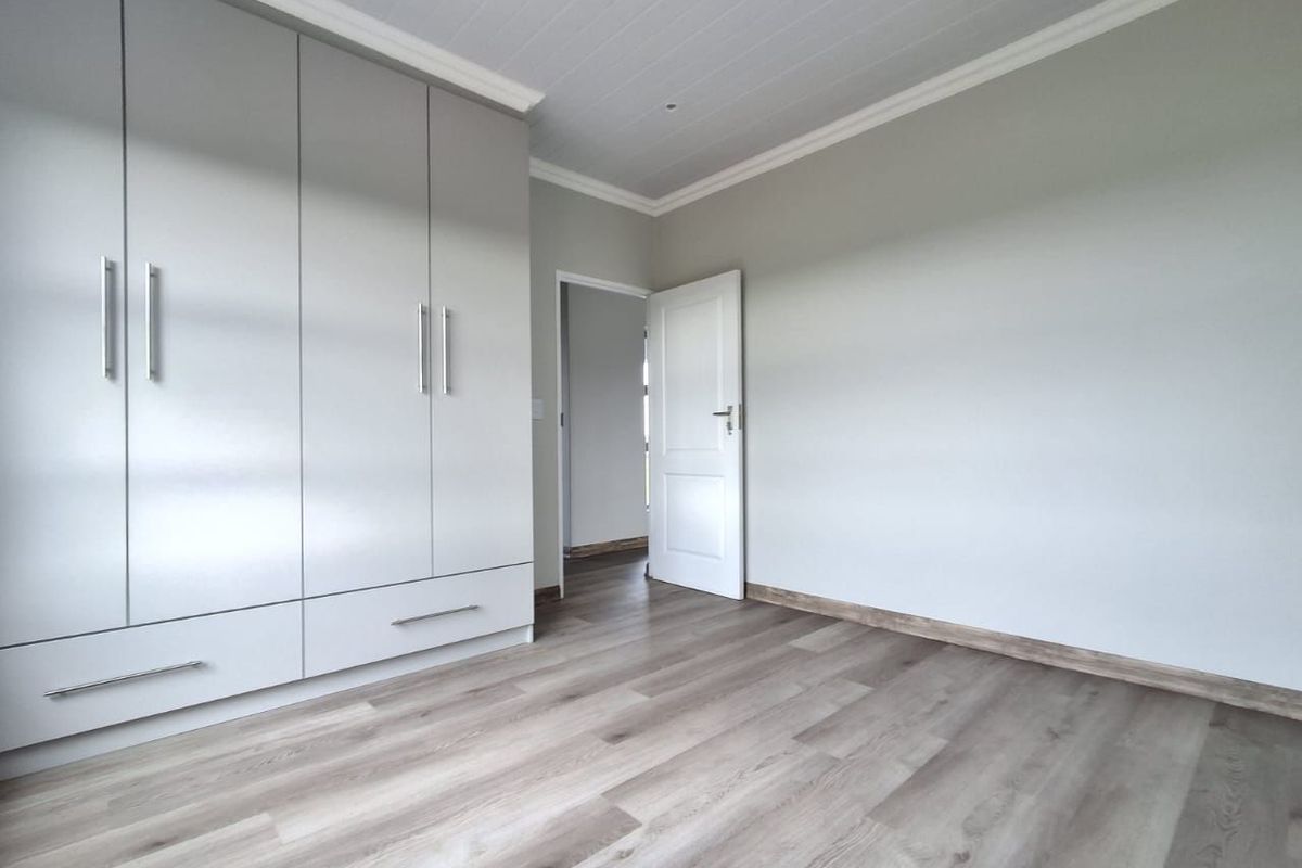 A bright, modern bedroom featuring neutral walls, light wood-look laminate flooring, and ample built-in cupboard storage with a clean, contemporary finish.
