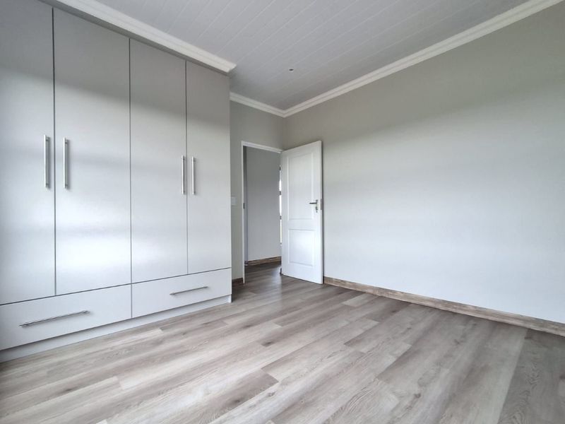 A bright, modern bedroom featuring neutral walls, light wood-look laminate flooring, and ample built-in cupboard storage with a clean, contemporary finish.