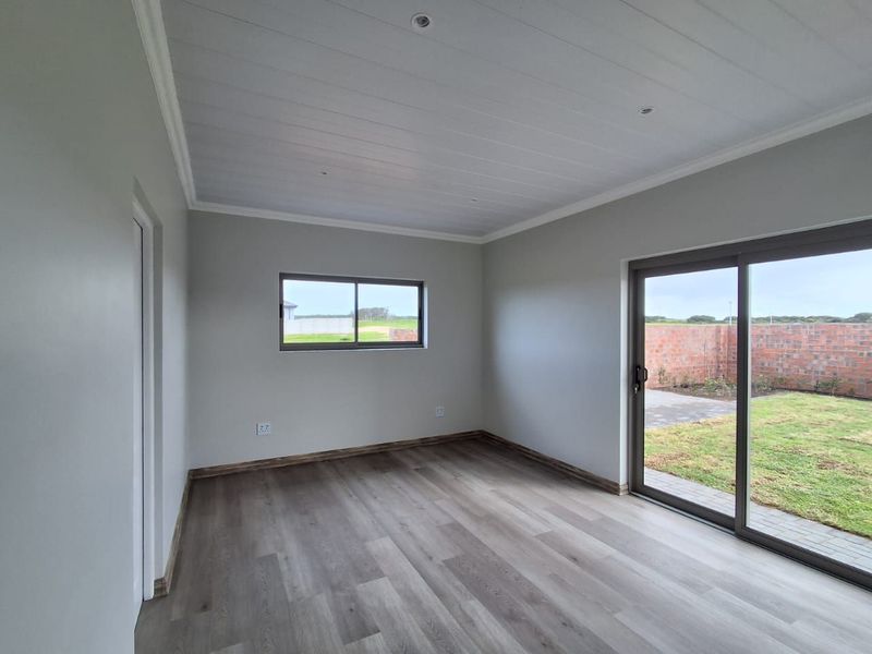 A bright, modern, and empty bedroom featuring laminate flooring, recessed lighting, and a sliding glass door providing direct access to the rear garden.