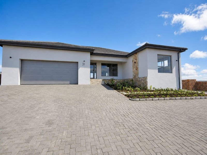 Modern single-story residential home featuring a paved driveway, double garage, and stone-clad architectural accents under a clear blue sky.