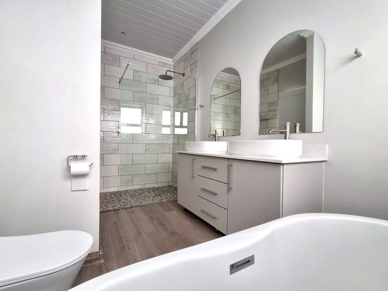 Modern bathroom featuring a double vanity with vessel sinks, a spacious walk-in shower with pebble flooring, and a sleek freestanding bathtub.