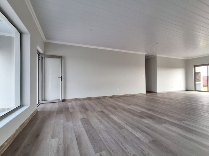 A spacious, bright, and empty living area featuring modern laminate flooring, a clean tongue and groove ceiling, and large glass doors providing natural light.