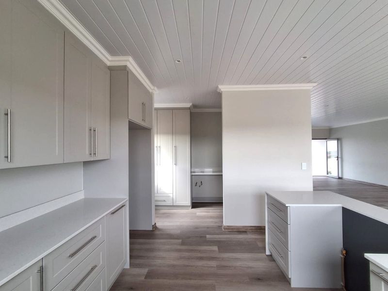 Modern, spacious kitchen featuring neutral cabinetry, stone countertops, and tongue and groove ceiling details, offering a clean and contemporary aesthetic.