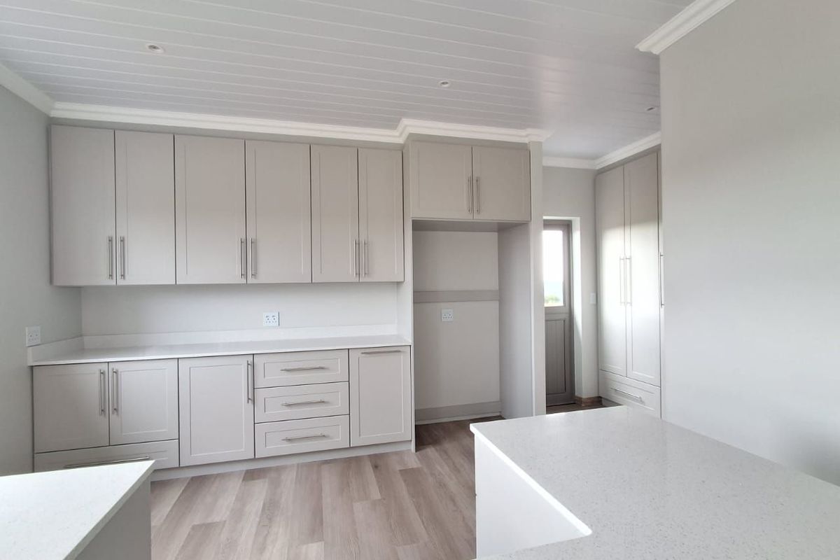 A modern, clean-lined kitchen featuring neutral shaker-style cabinetry, quartz countertops, and light wood-look laminate flooring with a bright, contemporary finish.
