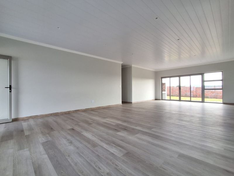 Spacious, light-filled living area featuring modern laminate flooring, a clean tongue and groove ceiling with recessed lighting, and large sliding glass doors.