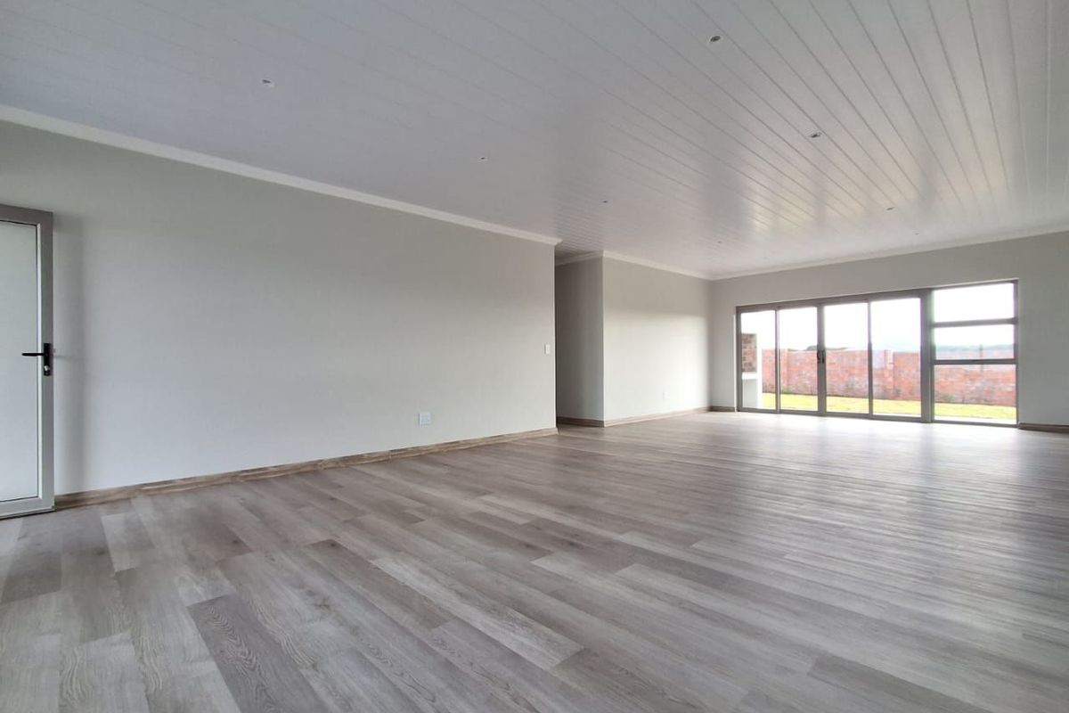 Spacious, light-filled living area featuring modern laminate flooring, a clean tongue and groove ceiling with recessed lighting, and large sliding glass doors.
